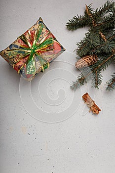 Blue fir tree branch with big cone, wrapped present box and cinnamon sticks on white wooden background. Christmas blank card, copy