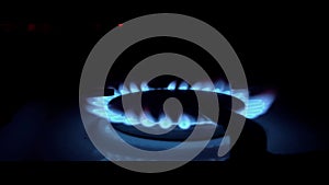 A blue fire lights up in the burner of the gas stove in complete darkness. The stove uses combustible or natural gas from the city