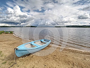 Blue fishing boat anchored on beach sand of lake. Smooth level