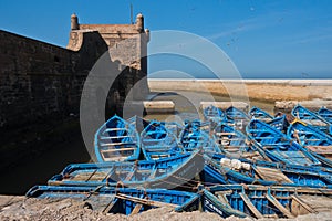 Blue fishing boats in Essaouira old harbor below Portuguese fortress Sqala du Port, Morocco