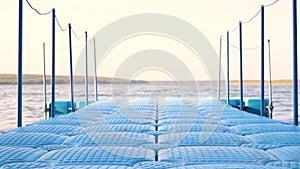 Blue floating plastic pontoon pier with rope railings rocking on waves at lake or river beach. Dock for small boats and