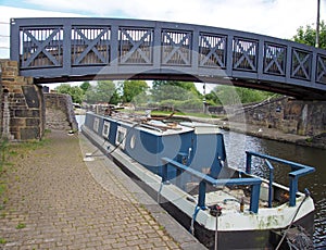 Blue footbridge crossing the calder and hebble navigation canal in brighouse west yorkshire with and old narrow boat moored