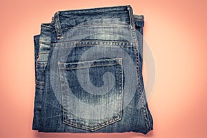 Blue frayed jeans with a pocket, folded shabby pants on a pink background. Dark denim