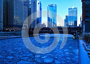 Blue and frigid winter morning in Chicago while el train passes over Chicago River and buildings reflect cityscape.