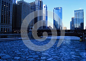 Blue and frigid winter morning in Chicago while el train passes over Chicago River and buildings reflect cityscape.