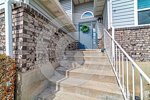 Blue front door with wreath and concrete stairs at the entrance of sunlit home