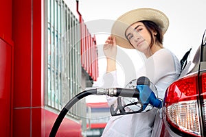 Blue fuel petrol pump nozzle against refueling auto car with petrol with beautiful female traveler waiting as blurred background