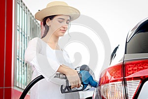 Blue fuel petrol pump nozzle against refueling auto car with petrol in beautiful young female traveler hand, beautiful young lady