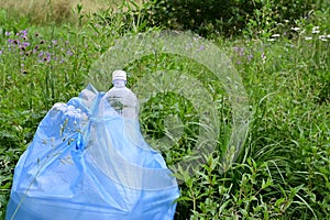 blue garbage bag filled with plastic bottles stands against background of green grass. Close-up. Protection of nature