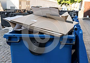 Blue garbage bin with cardboard in it in the city. Separate waste, preserve the environment concept. Segregate waste