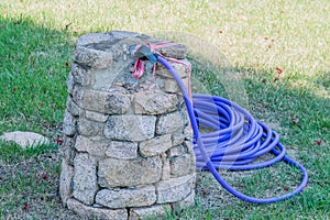 Blue garden hose coiled beside stone water tap