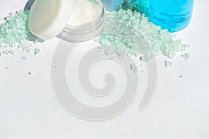 Blue gel in a bottle, white cup, blue bath salt, cream in a jar on a white background. Copy space