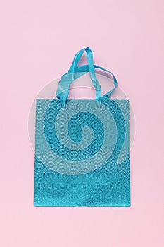 A blue gift bag with handles on a pink background