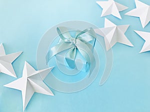 Blue gift box with blue ribbon on blue background with white star origami, diagonal.