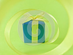 Blue gift box at the end of the spiral yellow ribbon, green background.