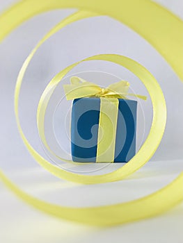 Blue gift box at the end of the spiral yellow ribbon, white background, vertical.