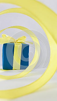 Blue gift box at the end of the spiral yellow ribbon, with white background, vertical.