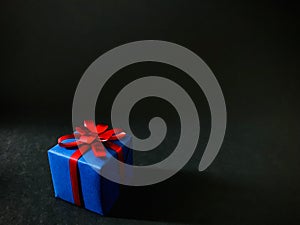A blue gift box with red ribbon on black background.