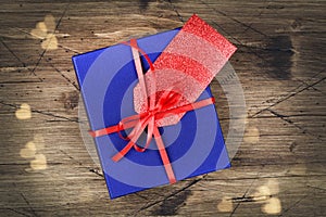 Blue gift box with red ribbon, blank gift tag and bokeh on wooden background.