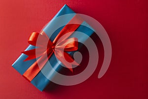 Blue gift box with red ribbon and bow isolated on red background, top view. Christms, party concept