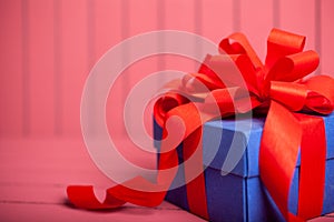 Blue gift box with red ribbon and bow on pink background