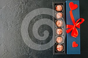 Blue gift box with red tape and chocolate on a black stone background