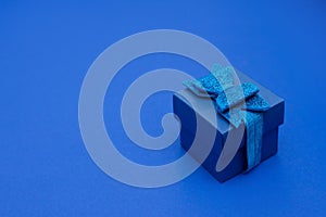 Blue gift box with ribbon, bow on classic blue background, copy space