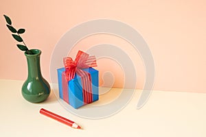 Blue gift box, vase of eucalyptus leaf, red colored pencil on ivory table. pink wall background