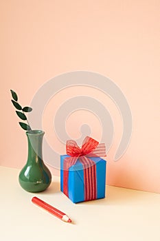 Blue gift box, vase of eucalyptus leaf, red colored pencil on ivory table. pink wall background