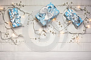 Blue gift boxes and lights with pearls on white wooden background