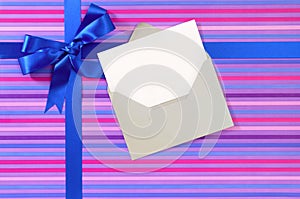 Blue gift ribbon bow on candy stripe wrapping paper, blank Christmas card, copy space