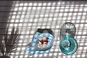 Blue glass of clean water and pills on white marble background with shadows from sunlight. Concept for pharmacy, medical dietic