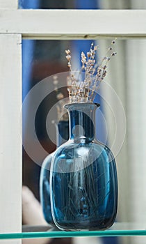 A blue glass vase with a dry plant is on the shelf.