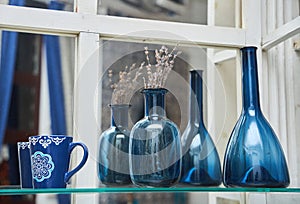 A blue glass vase with a dry plant is on the shelf.