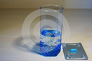 Blue glass with water and one blue pill in plastic round pill box on wooden background