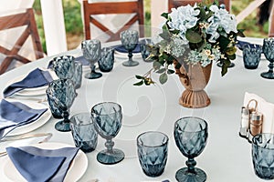 Blue glasses, plates and utensils on a festive table with flowers.