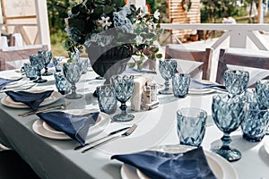 Blue glasses, plates and utensils on a festive table with flowers.