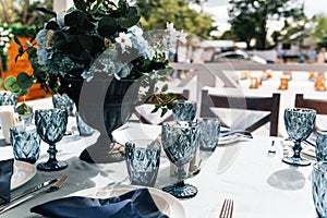 Blue glasses, plates and utensils on a festive table with flowers.