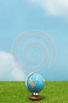 Blue globe on green grass over blue sky background.