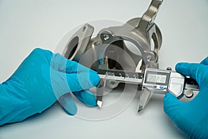 Blue gloved hand of engineer measuring metal parts with digital vernier caliper in workshop