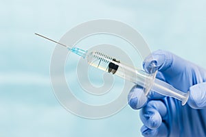 Blue gloved hand holding a syringe on blue background