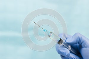 Blue gloved hand holding a syringe on blue background