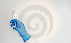 A blue-gloved hand holds a syringe on white background