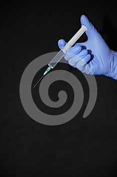 Blue gloved hand, protect against coronavirus COVID-19, holding a syringe, filled with a transparent liquid, down