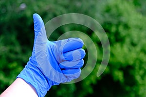 Blue gloved hand, raised thumbs up, closed point, on green background