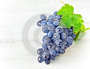 Blue grapes with green leaf on wooden board