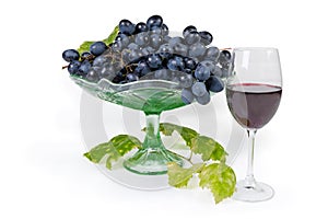 Blue grapes on vintage fruit vase, vine twig, red wine