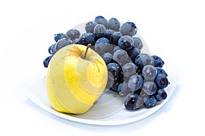 Blue grapes with yellow apple on a white plate