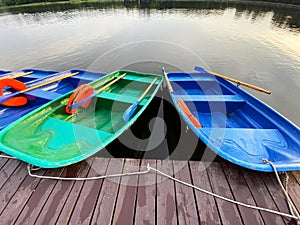 Blue and green boats with oars and orange lifebuoys are moored to a wooden pier