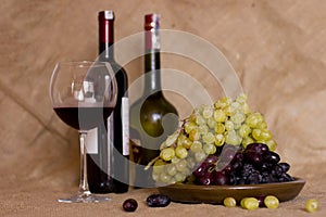 Blue and green grapes on a clay brown dish. Bottle with red and